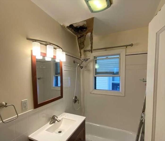 A large hole in a bathroom ceiling with staining and hanging debris
